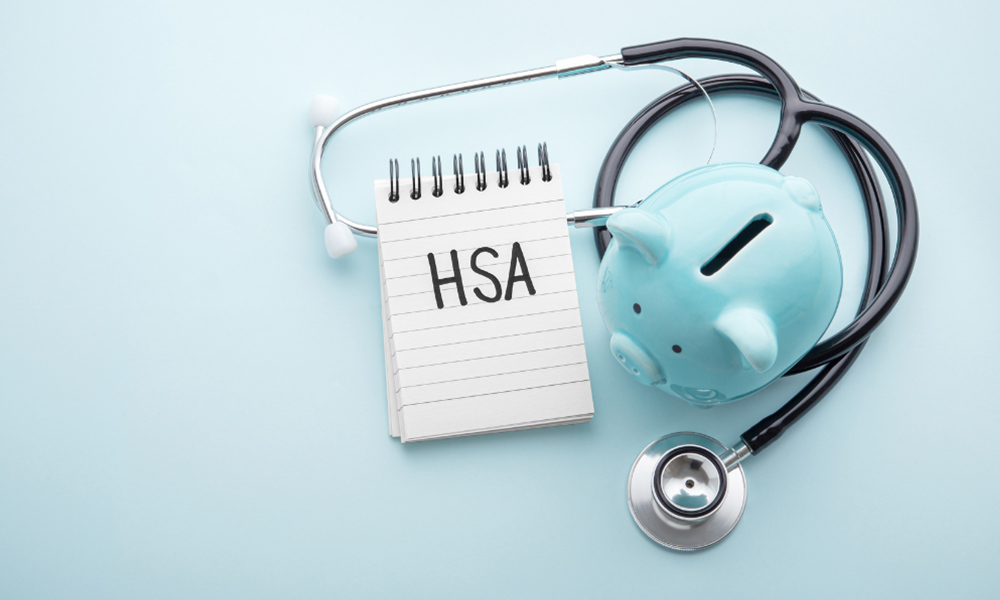 Blog - Blue Background with a Top Down View of a Blue Piggy Bank Sitting on Top of a Stethoscope Next to a Notebook with HSA Written on it